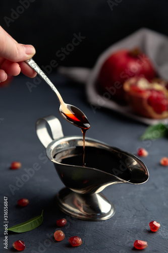 Pomegranate sauce flows down from a spoon in a gravy boat on a dark background