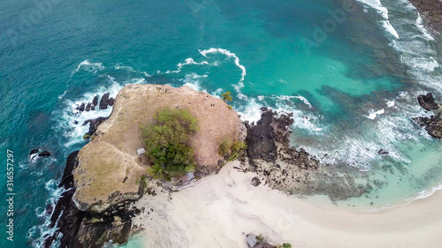 A top-down drone shot of an idyllic Koka Beach. Hidden gem of Flores, Indonesia. Headland going straight into the open sea. Beauty in the nature. Calm waves washing the cliff's slopes. Serenity. photo