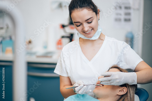 Canvas Print careful professional dentist in white uniform treating patient's teeth, making p