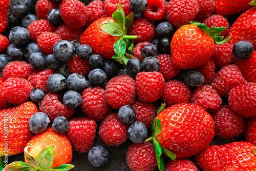 Closeup photo of freshly picked berries. On the photo there are a mix of berries: blueberry, wild strawberry and raspberry. Red, blue and purple colors on background