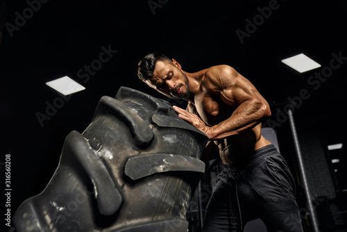 Man moving giant tire in gym.