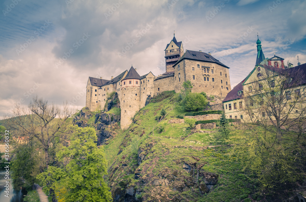 Loket Castle Hrad Loket gothic style building on massive rock over Eger river and colorful buildings in Loket town, green trees and hills, Karlovy Vary Region, West Bohemia, Czech Republic