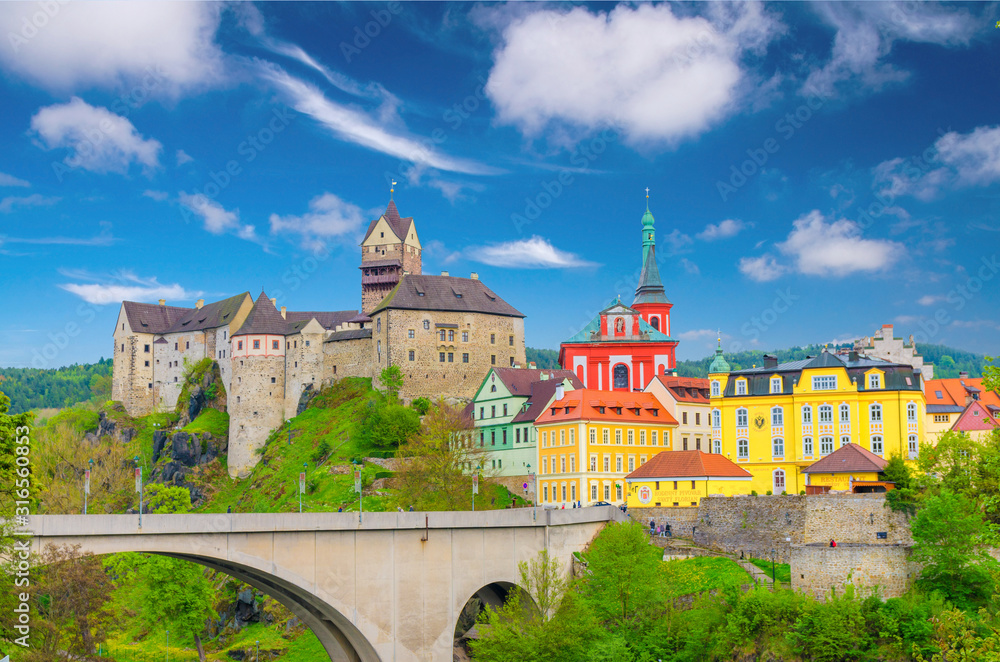 Loket Castle Hrad Loket gothic style building on massive rock, colorful buildings in town, bridge over Eger river, blue cloudy sky background, Karlovy Vary Region, West Bohemia, Czech Republic