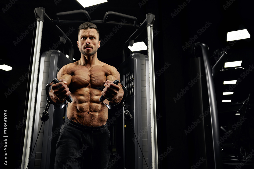 Shirtless bodybuilder doing low cable crossover exercise. Shirtless bodybuilder doing low cable crossover exercise.