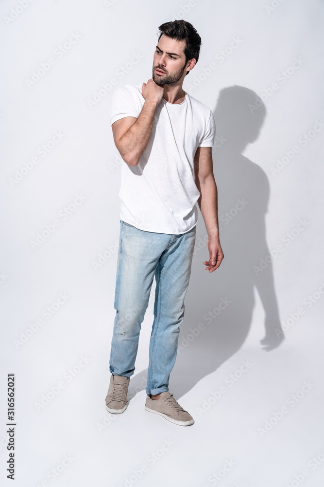 Full length of handsome young man in casual wear looking away and smiling while standing against grey background Full length of handsome young man in casual wear looking away and smiling while standing against grey background
