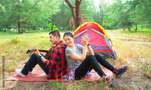 Romantic couple camping outdoors and sitting at tent. Happy couple on a romantic camping vacation. Couple asian camp forest adventure and playing guitar together in nature. Travel in summer holiday
