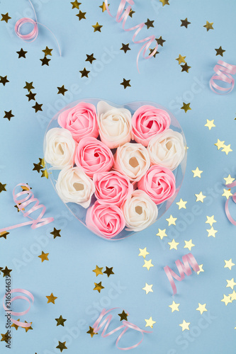 white and pink candy in form of roses in box , pink ribbon and small stars on blue background.