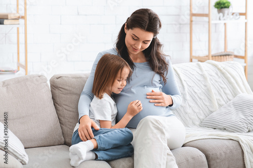 Curious little girl observing her pregnant mother tummy photo