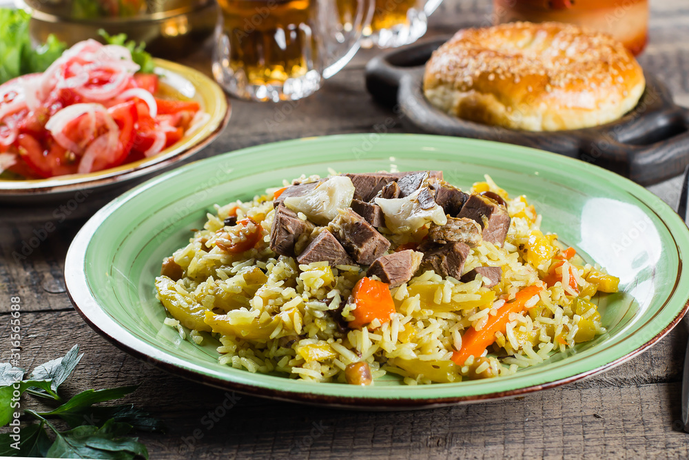 National Traditional Uzbek pilaf with meat and rice on a wooden table. Oriental cuisine concept. Close-up image National Traditional Uzbek pilaf with meat and rice on a wooden table. Oriental cuisine concept. Close-up image