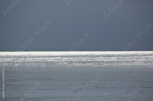 Seascape in grey / gray, shining bright steel / silver colorf of sea, horizon, dark gray sky, concept of calm, peaceful view