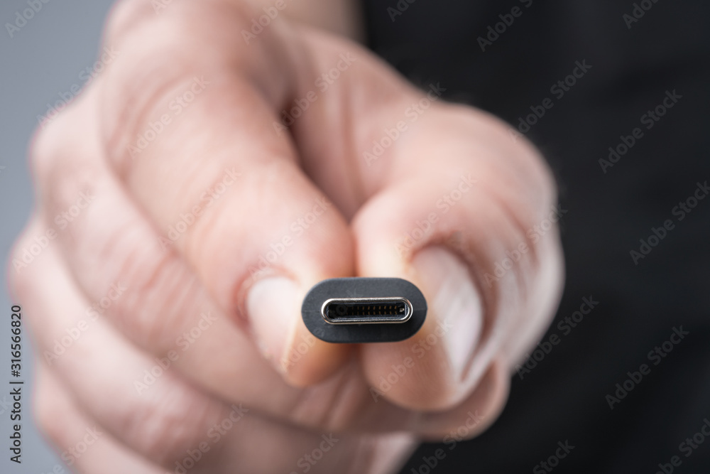 USB Type C connector with a grey cable being held in hand. Shallow depth of field.