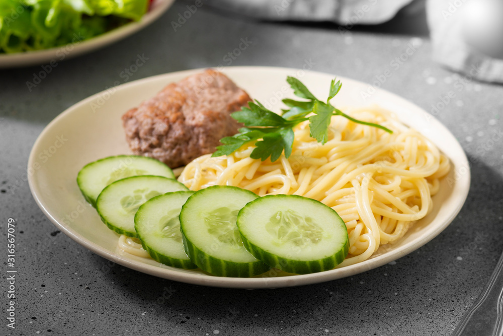 Pasta, cutlet and cucumbers on a beige plate on a gray table Pasta, cutlet and cucumbers on a beige plate on a gray table