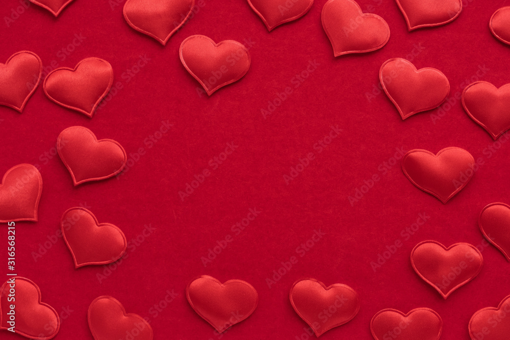 Small textile red hearts are on a background of red velvet paper.