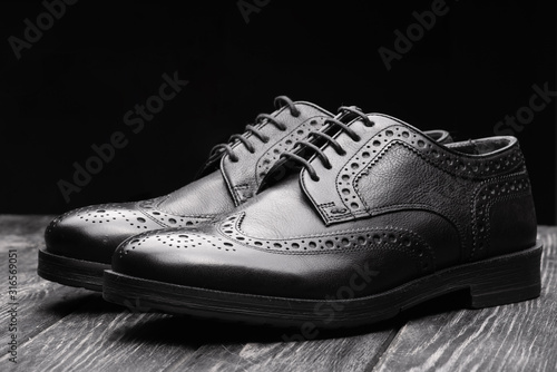 Black leather shoes against wooden background.