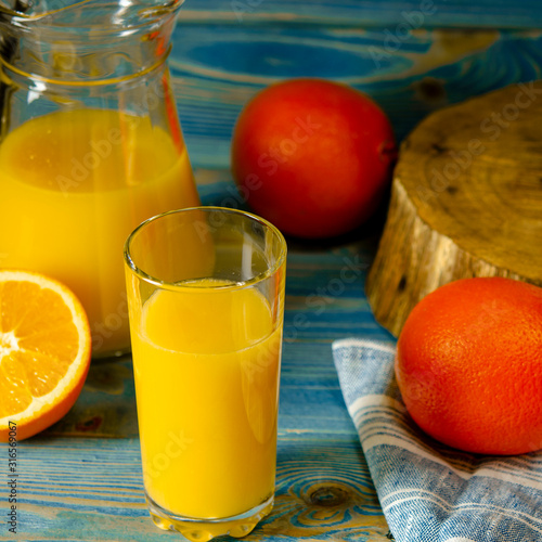 Glass and pitcher of orange juice on wooden table, on green background