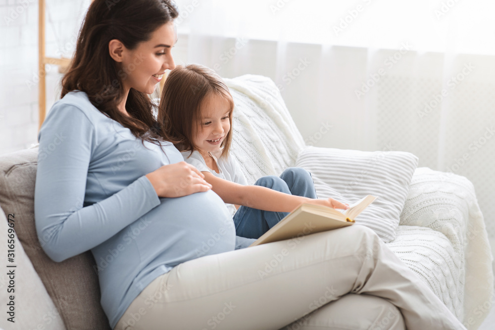 Little girl and pregnant mother enjoying book together