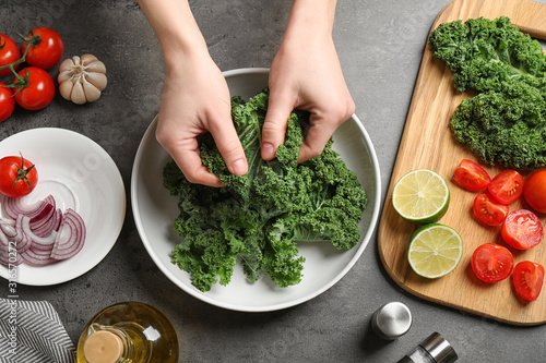 Woman cooking tasty kale salad on grey table, top view
