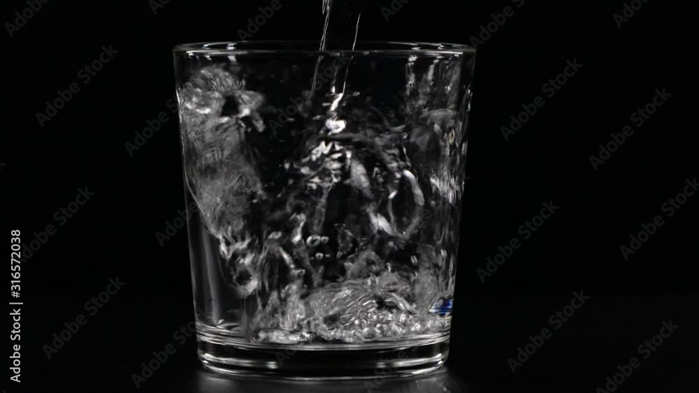 Slow motion pouring water in a glass on black background with splash, drops and bubbles Slow motion pouring water in a glass on black background with splash, drops and bubbles