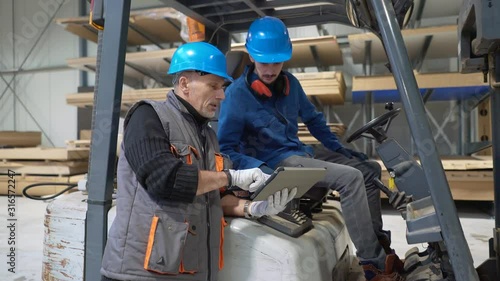 Man giving instructions to apprentice in warehouse, using cart photo