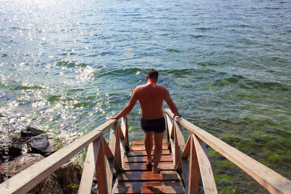 A man goes down a wooden staircase to the lake. Bathhouse on the shore of a pond. Background. A man goes down a wooden staircase to the lake. Bathhouse on the shore of a pond. Background.