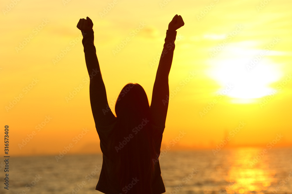Happy woman raising arms at sunset on the beach