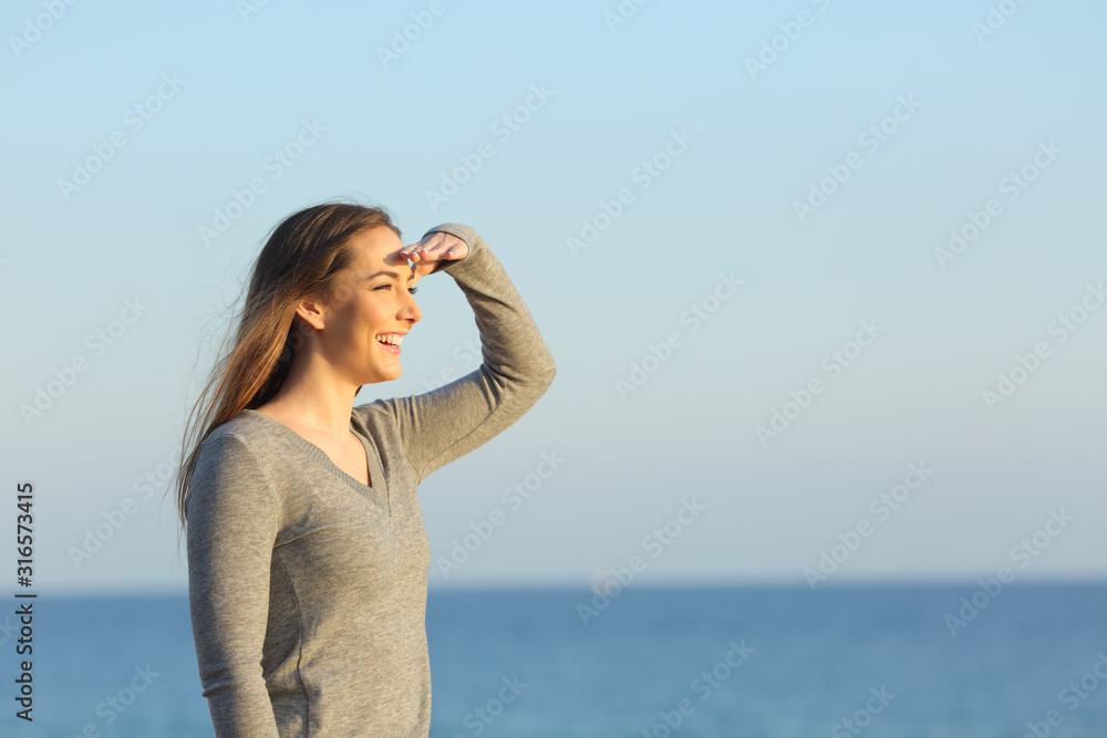 Happy woman searching on the beach with hand on forehead