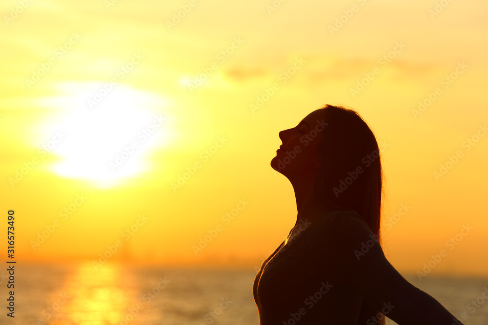 Woman silhouette breathing fresh air at sunset on the beach