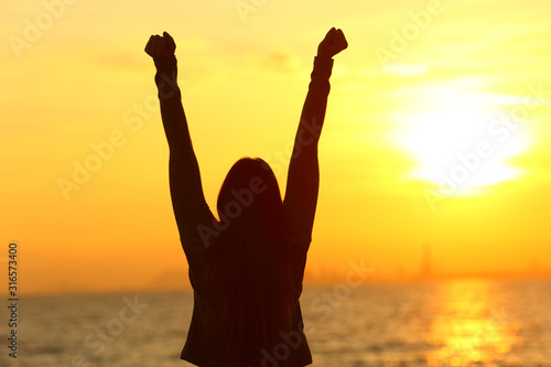 Happy woman raising arms at sunset on the beach