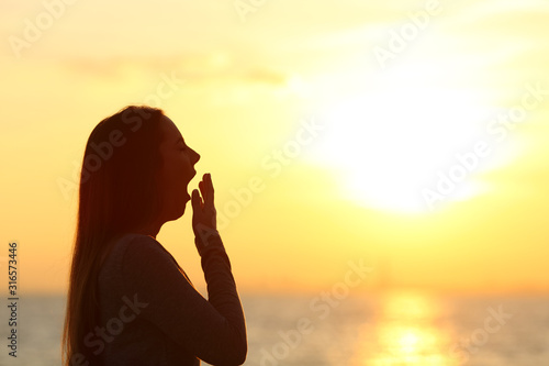 Tired woman yawning at sunset on the beach