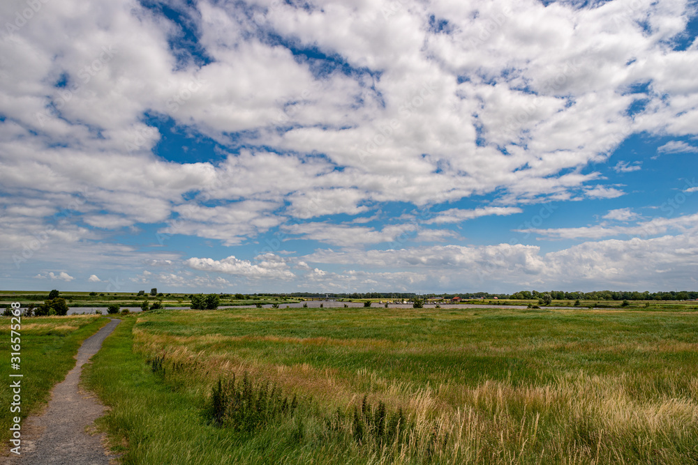 Scenic marsh landscape with view over a sewer with Marina in the background and wonderful white clouds in the blue sky, Greetsiel, Lower Saxony, North Germany