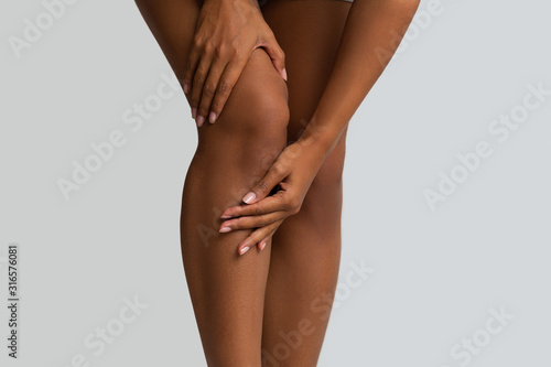 Black woman massaging her painful knee, close up