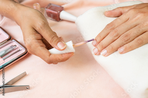 Female hands doing nail polish in pearl pink color with set of manicure instruments and tools  on pink silk velvet. beauty  manicure concept
