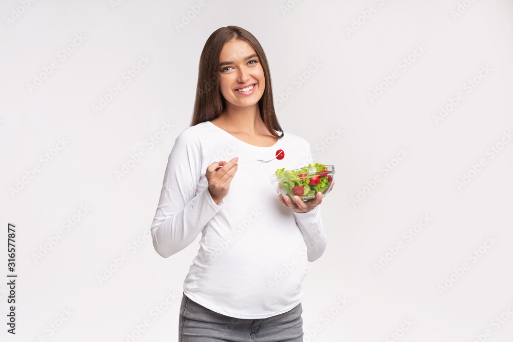 Happy Pregnant Woman Eating Salad Standing On White Background, Studio Happy Pregnant Woman Eating Salad Standing On White Background, Studio