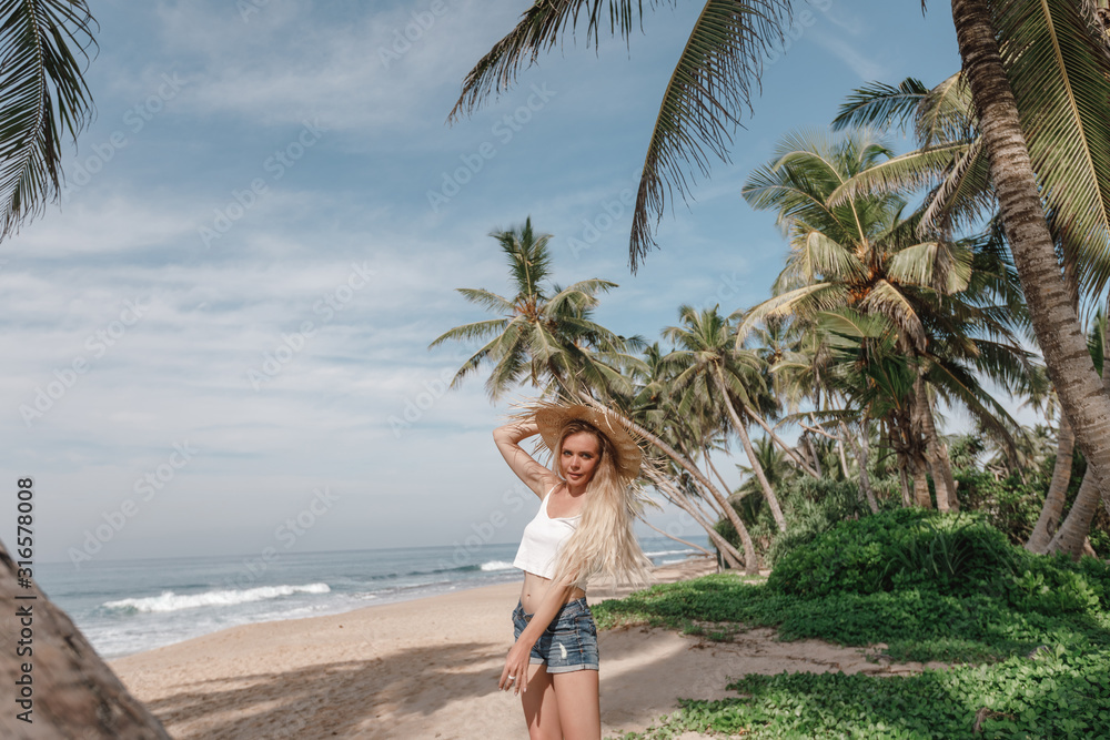 Lifestyle Image of carefree traveling smiling woman in white top and straw hat spending her leisure time on the beach . Summer mood.