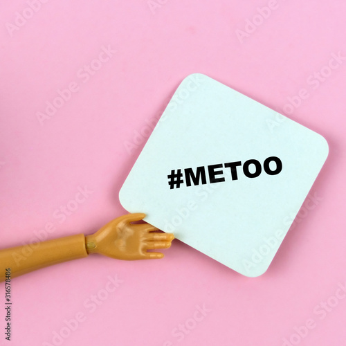 Fotografie hand of a plastic doll with sign me too  on a pink background