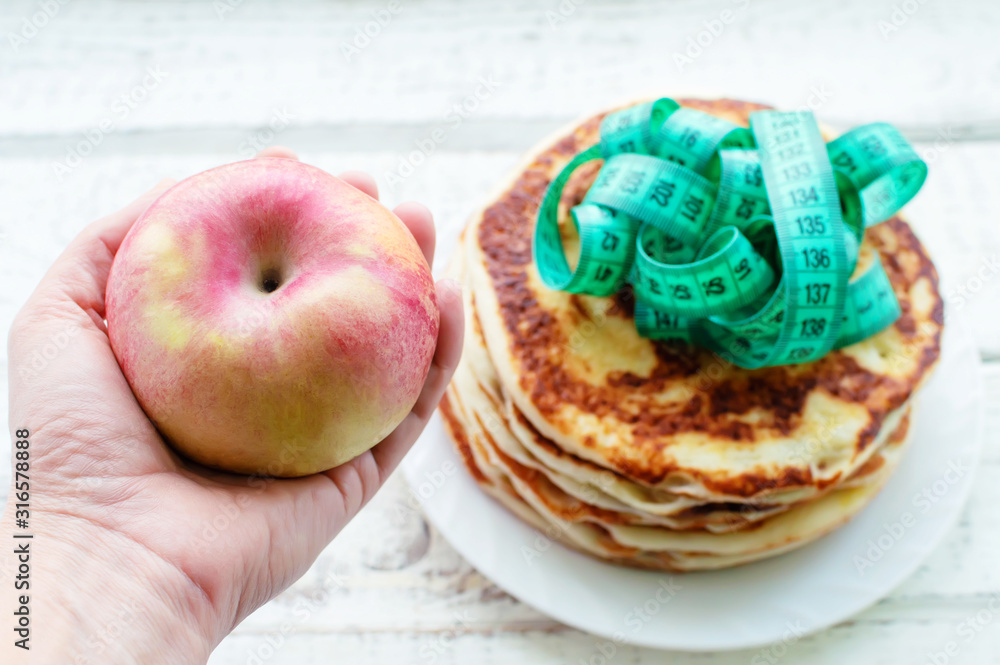 hand holding a red Apple on a background of pancakes with a centimeter tape. the concept of a healthy lifestyle. the fight against excess weight. hand holding a red Apple on a background of pancakes with a centimeter tape. the concept of a healthy lifestyle. the fight against excess weight.