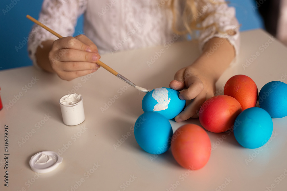 preparation for the holiday of Easter: the child paints with white paint colored Easter eggs, a brush in children's hands. preparation for the holiday of Easter: the child paints with white paint colored Easter eggs, a brush in children's hands.