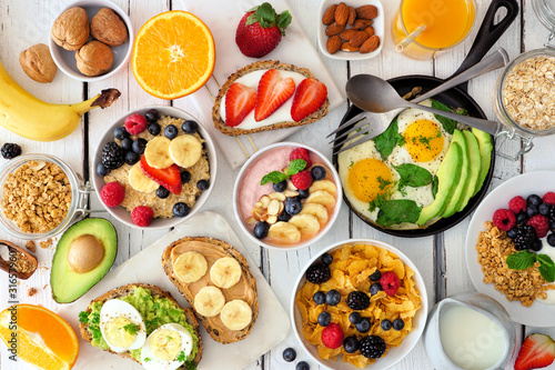Healthy breakfast table scene with fruit, yogurts, oatmeal, smoothie bowl, cereal, nutritious toasts and egg skillet. Top view over a white wood background.
