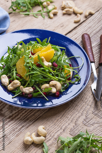 Vegan plant based salad with fresh arugula, orange, pomegranate seeds, cashews