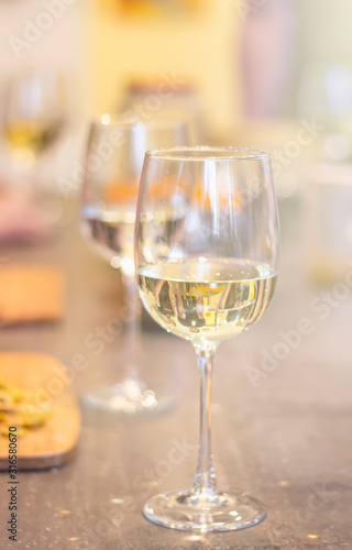 Refreshing white wine in glasses standing side by side on a table with candle in the sun light, blurred background.