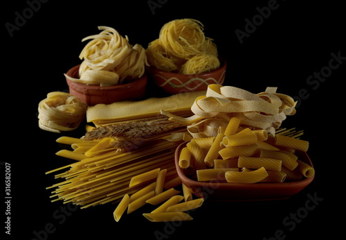 Uncooked Italian tagliatelle, spaghetti, lasagna, pappardelle, penne rigate, tortiglioni or elicoidali, fidellini or egg pasta isolated on black background photo