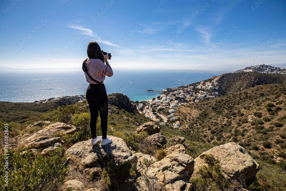 Beautiful woman photographer standing on a cliff taking a picture with a professional camera