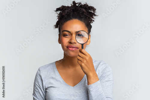 Suspicious young woman looking at camera through magnifier