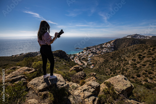 Beautiful woman photographer standing on a cliff holding a professional camera