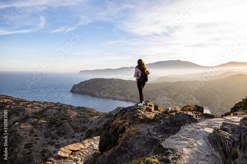 Beautiful woman standing on a cliff during sunset with the mediterranean sea in the background at Cap de Creus photo