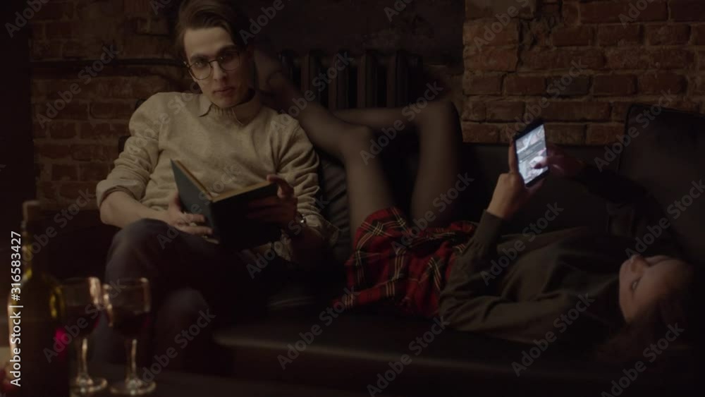 Couple at sofa reading books and social media in stylish loft studio. Shallow depth of field Couple at sofa reading books and social media in stylish loft studio. Shallow depth of field