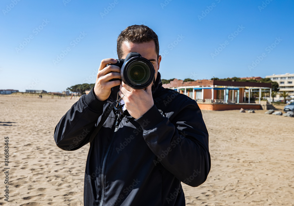 Young man taking a picture with a DSLR camera front shot at the beach Young man taking a picture with a DSLR camera front shot at the beach