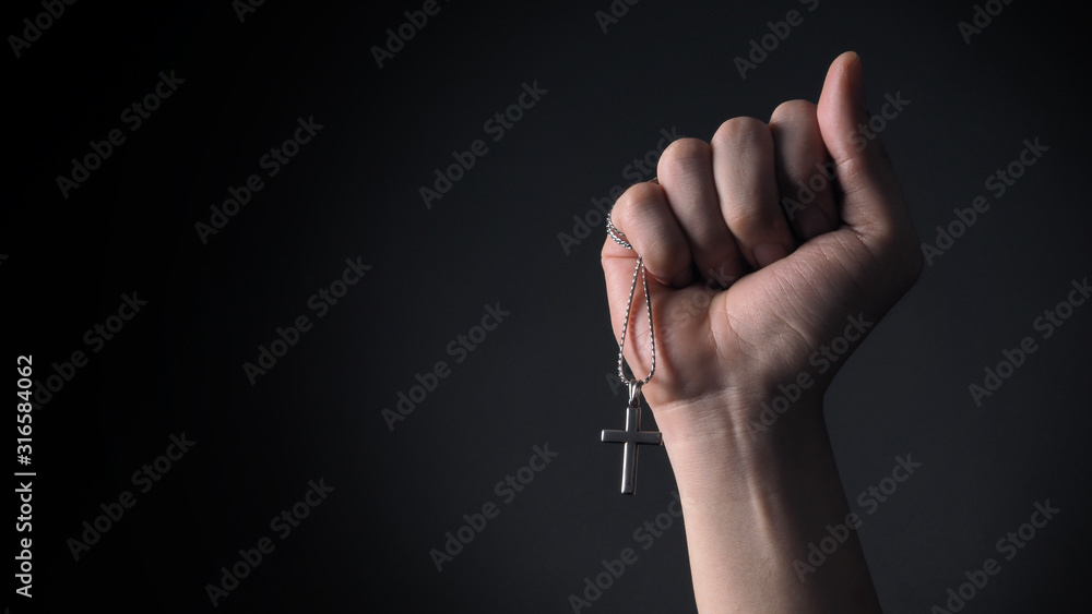 Close-up images of crucifix pendant and necklace in hand on black color background in studio which represent praying for god or jesus and thank gods for giving peaceful and faithful to people