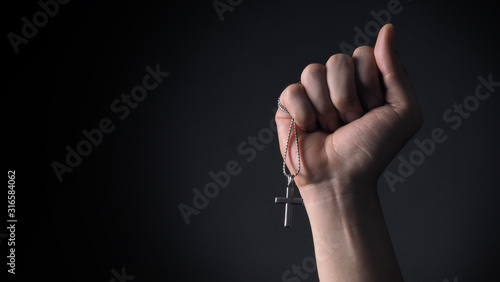 Close-up images of crucifix pendant and necklace in hand on black color background in studio which represent praying for god or jesus and thank gods for giving peaceful and faithful to people