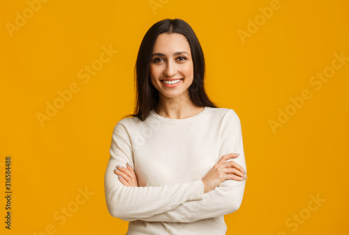 Beautiful brunette woman standing with folded arms over yellow background